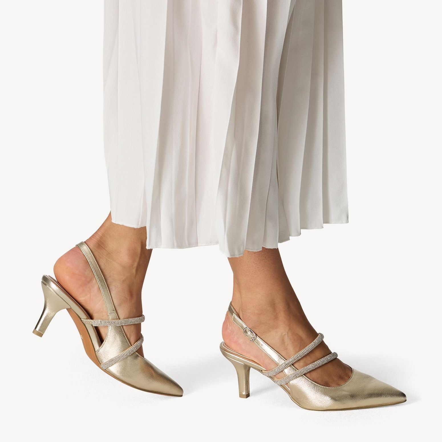 Gold high-heeled shoes worn with white pants on a white background