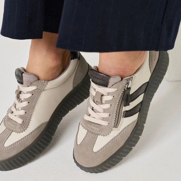 A close-up of a person wearing low-top platform sneakers in taupe, cream, and black, paired with dark navy pinstriped trousers.