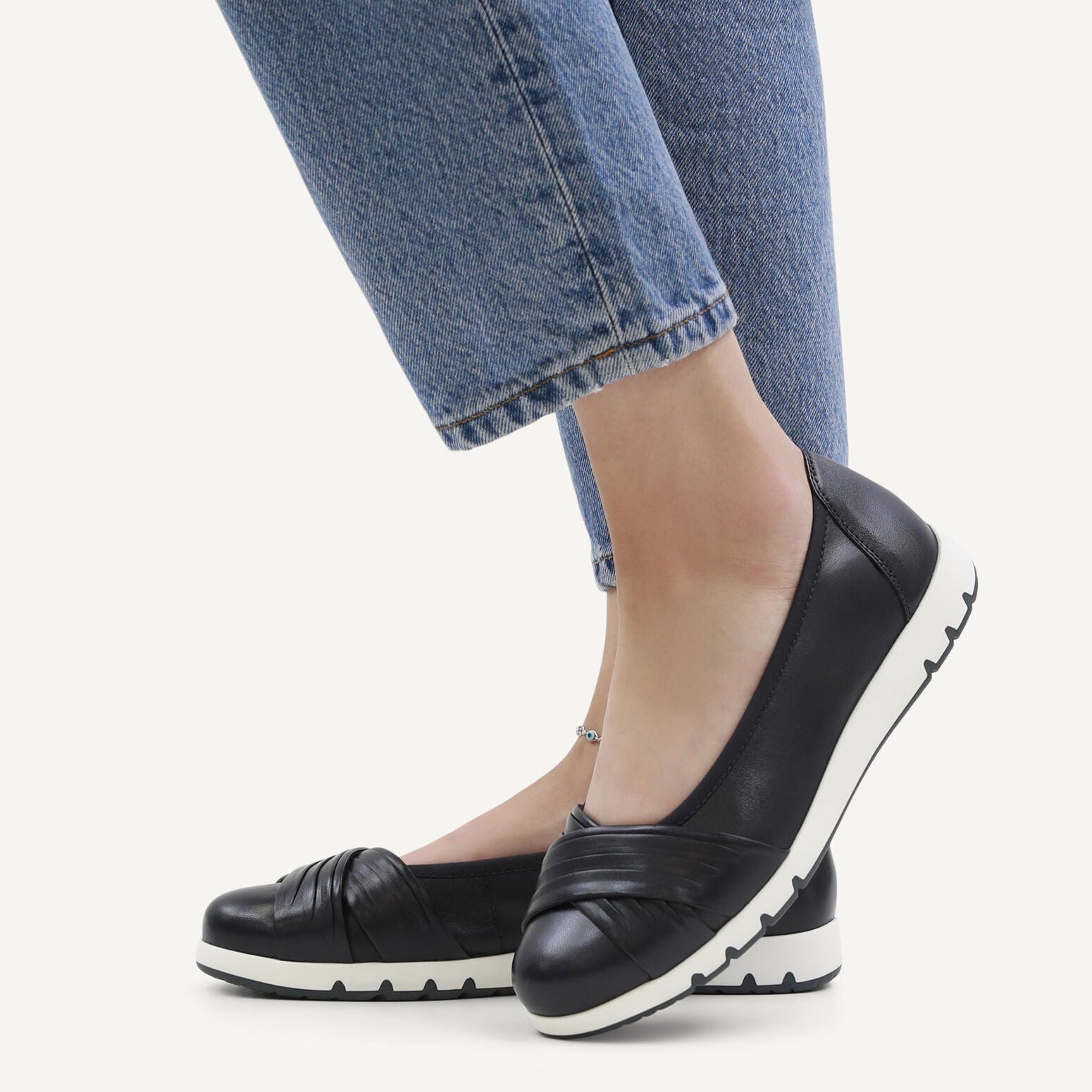 Navy flat shoes worn with blue jeans on a white background