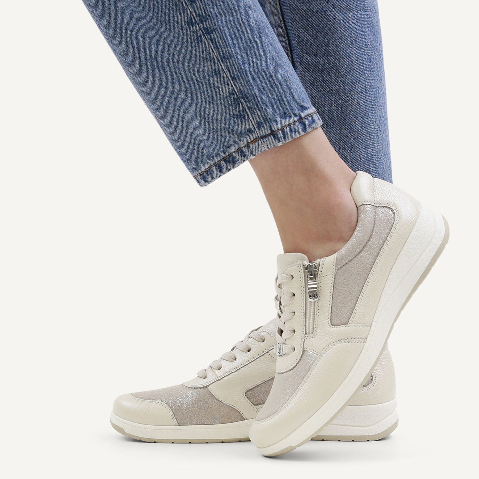 Light gray sneakers worn with blue jeans on a white background