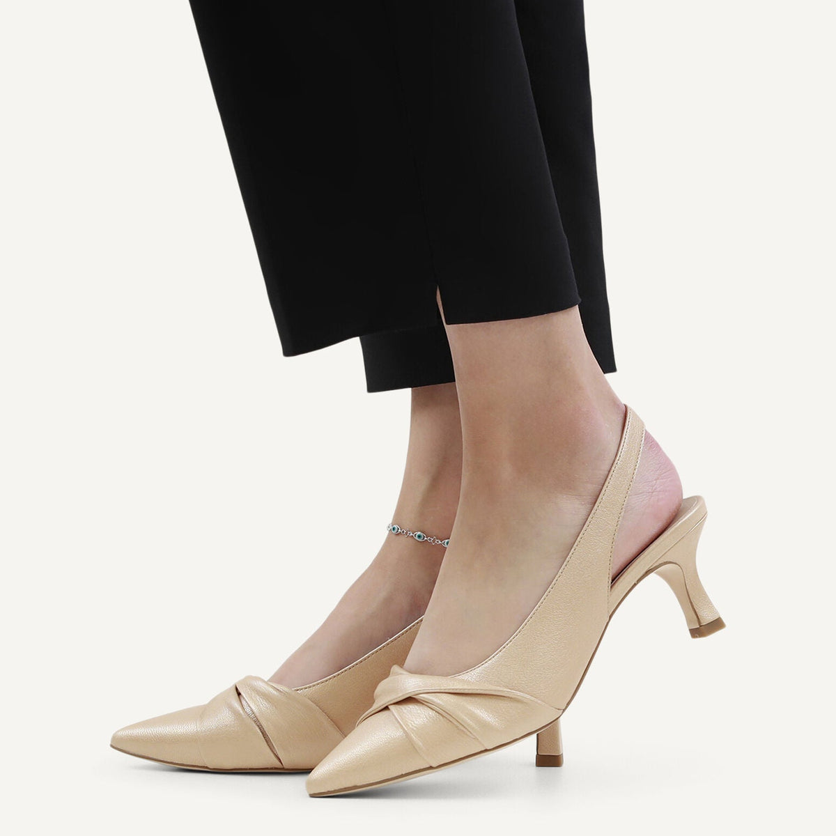 Beige high-heeled shoes worn with black pants on a light background