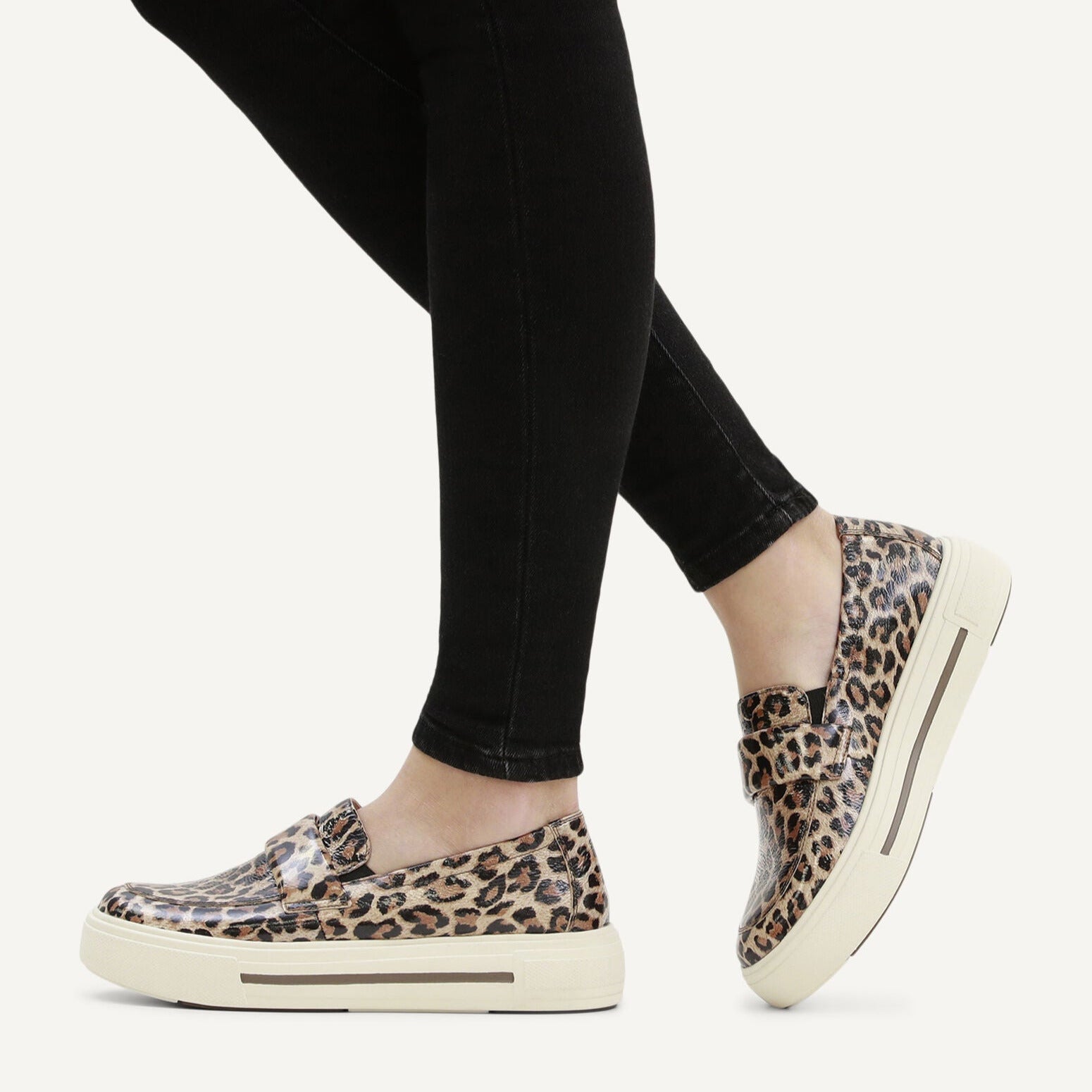 Person wearing leopard print slip-on shoes with black leggings on a white background