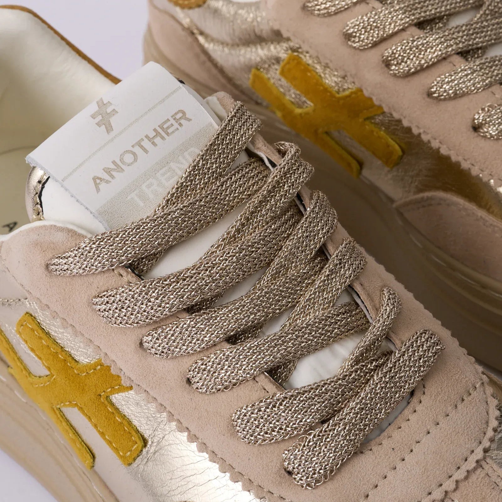 Beige sneakers with gold accents and 'Another' branding on a white background