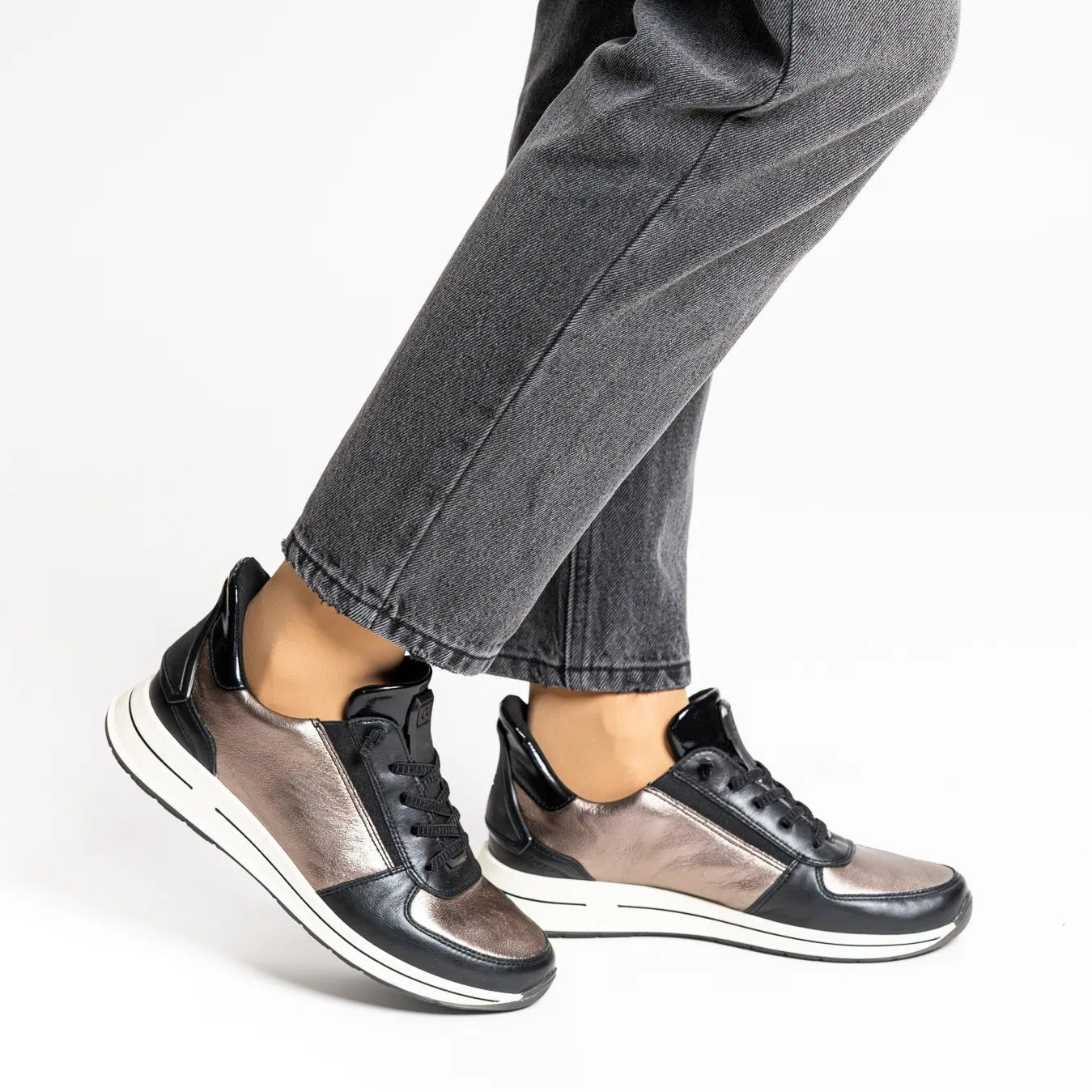Person wearing black and gray sneakers with rolled-up jeans on a white background
