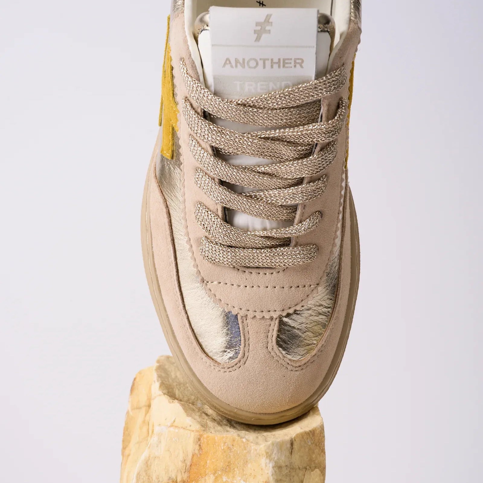 Beige sneaker with a brand label on a wooden block against a light gray background
