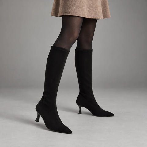 Miss Elastic Zeta black stretch knee-high boots styled with a camel skirt and black tights in a grey studio
