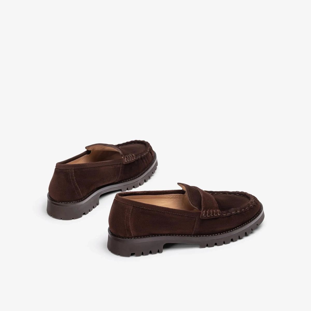 A pair of dark brown suede penny loafers with rugged, lug soles, shown from a three-quarters angle on a light gray background.