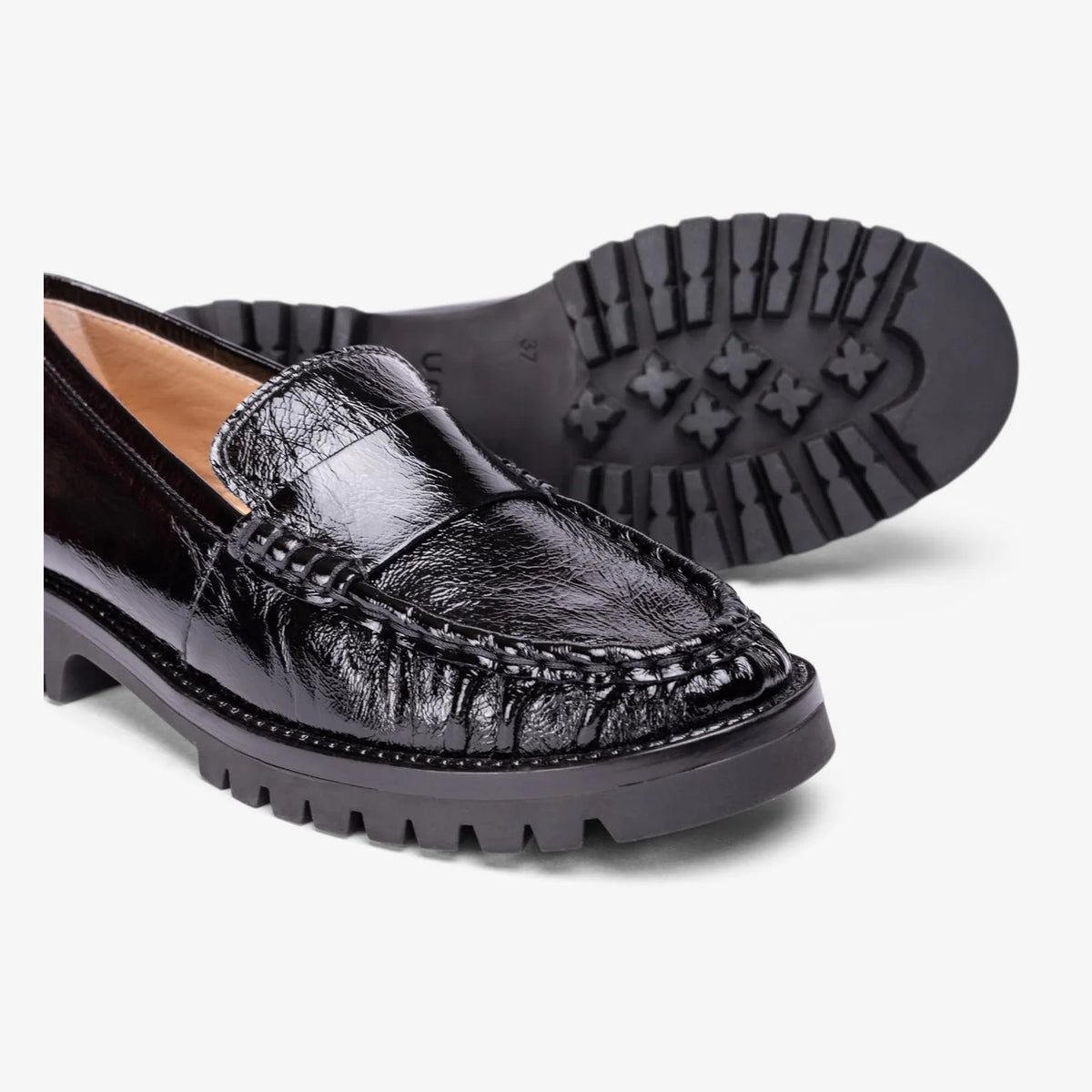 Close-up of Unisa Fijo black patent leather stitching beside the treaded outsole.
