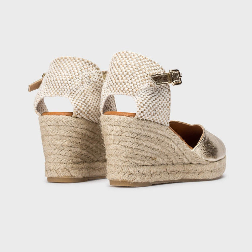 Pair of gold wedge sandals with espadrille sole on a white background